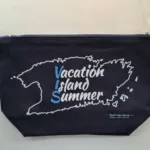Tamnoplava torbica s patentnim zatvaračem, ukrašena bijelim tiskom konture otoka i natpisom "Vacation Island Summer". Dizajn uključuje modernu tipografiju i promovira ljetne motive. Torbica je minimalistička i praktična, idealna za plažu ili svakodnevnu upotrebu.