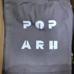 Siva platnena torba s minimalističkim tiskom bijelog teksta POP ARH. Torba je praktična, modernog dizajna, pogodna za nošenje knjiga, dokumenata ili svakodnevnih predmeta.