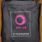 Crna platnena vrećica s tiskanim logotipom u ružičastoj boji koji prikazuje stilizirano slovo C unutar kruga. Ispod logotipa nalazi se natpis JVC-19 u ružičastoj boji, a ispod toga bijelim slovima piše: "19th Joint Vacuum Conference" te datum i lokacija događaja: 29.9. - 4.10.2024. Podstrana, Croatia.